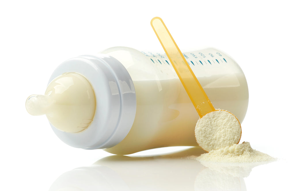Bottle of breastmilk laying on the side with a scoop of powdered milk. 